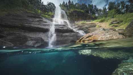 Enchanting-over-under-view-of-a-shallow-river-with-transparent-waters-and-a-distant-waterfall