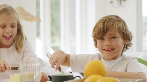 niño y niña con pijama divirtiéndose en la mesa de desayuno familiar haciendo cara con panqueque