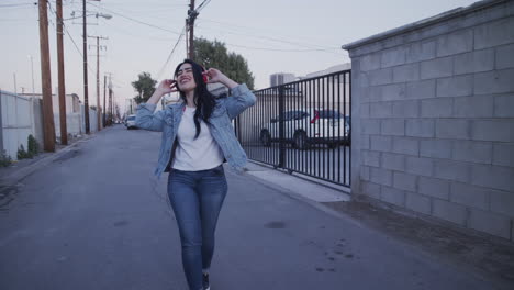 happy young women listen up to music walking through the alleyway wearing red headphones