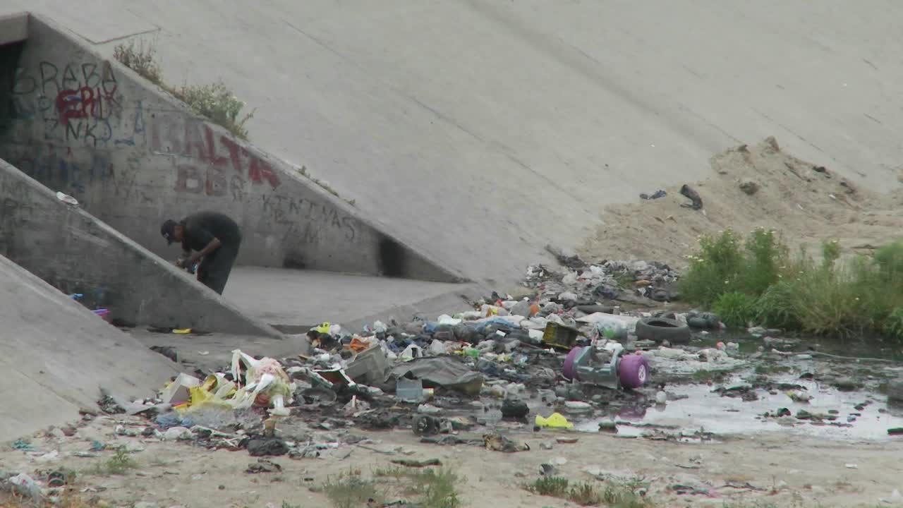 un hombre camina entre basura y basura en una zanja de drenaje