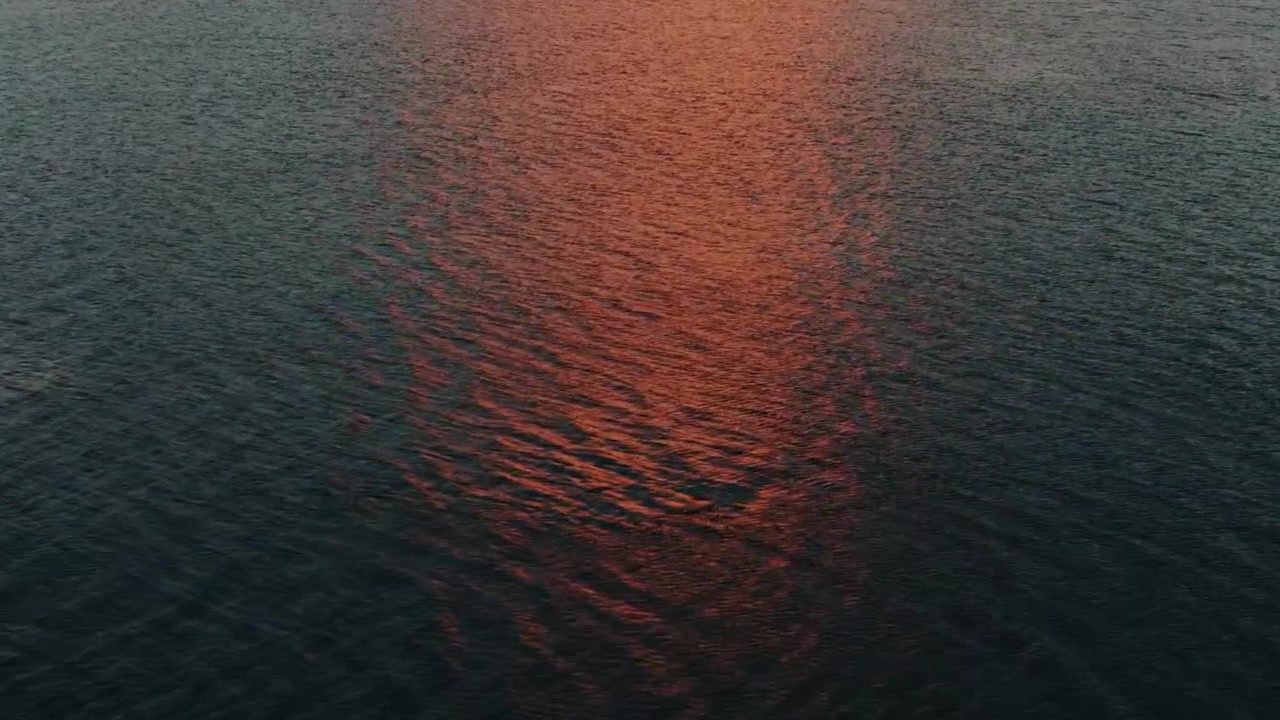 Aerial over Rippling Sea Reflecting Orange Sunset