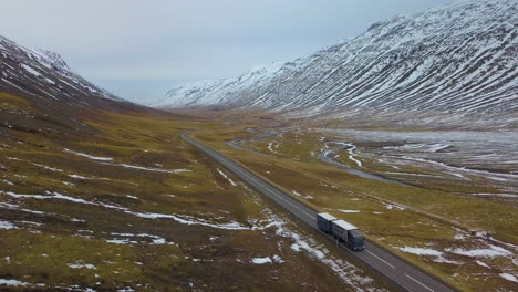 aerial view of transport truck driving down highway in between snowy mountains