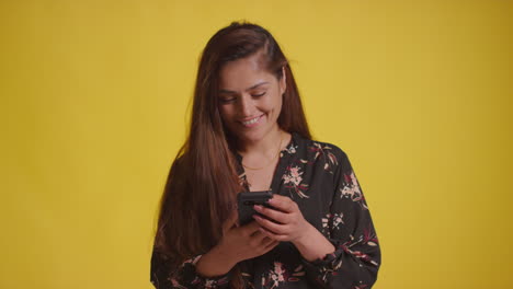 studio shot of smiling woman with mobile phone getting good news against yellow background
