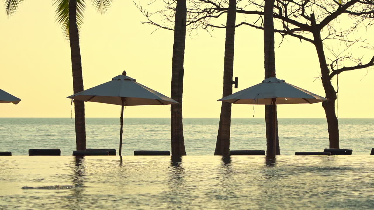 курорт с видом на море, бассейном-инфинити и зонтиками от солнца на закате