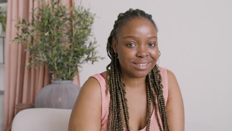 Woman-With-Braids-Sitting-On-A-Sofa-Smiling-And-Looking-At-Camera