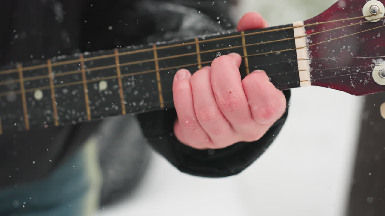 mano tocando la guitarra en cuerdas de polvo de nieve, mostrando la armonía de la música y la belleza del invierno, texturas heladas en la manga negra y el cuello de la guitarra