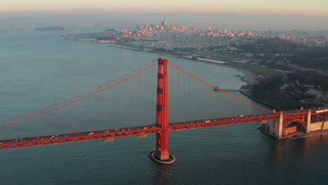 wide circling aerial shot of the golden gate bridge at sunset with san francisco skyline in the background