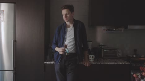 man standing in the kitchen thinking while eating chocolate bar