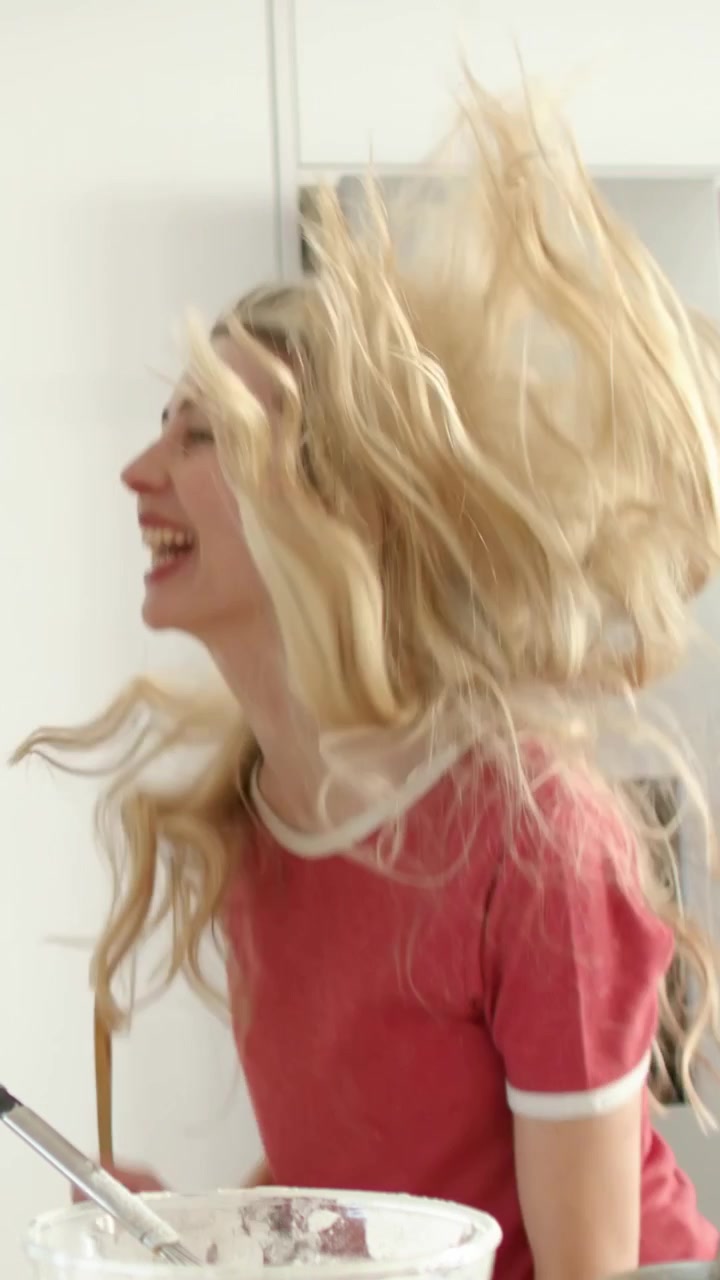 Video vertical: Mujeres cantando con camisetas amarillas y rojas, haciendo mímica mientras hornean en la cocina usando cucharas.