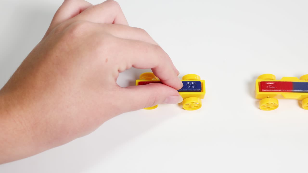 Hands manipulate colorful magnetic toy cars on a white surface, illustrating magnetic attraction and repulsion in a playful setting