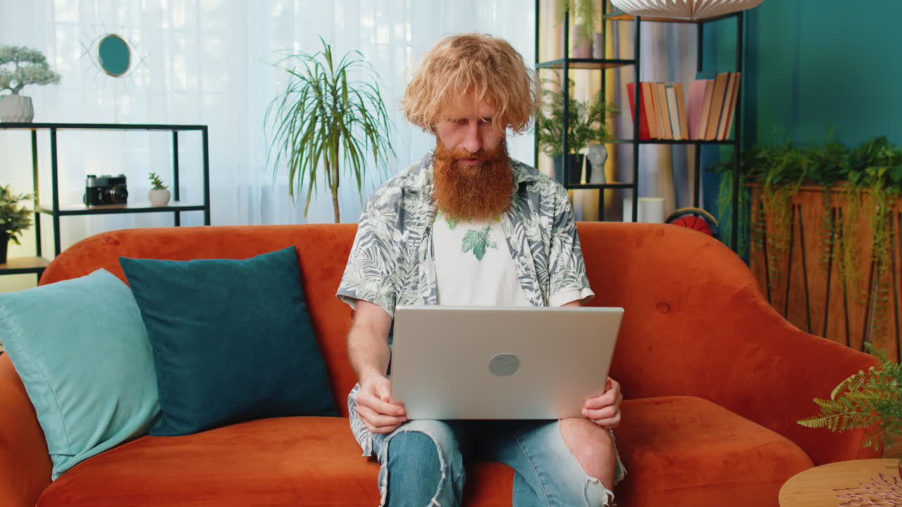 Redhead man freelancer starts working on laptop sends messages makes online purchases at home