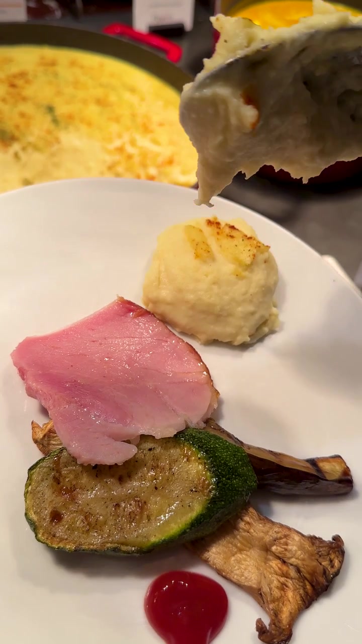 Una cuchara de metal saca puré de patatas cremoso de una olla roja a un plato.