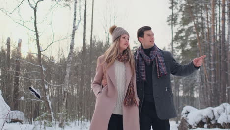 young married couple walks through the winter forest. a man and a woman look at each other laughing and smiling in slow motion.