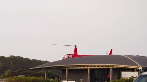 red helicopter lifting off from a helipad