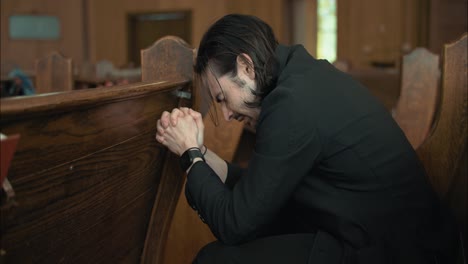 young man in black suit praying in church in cinematic slow motion