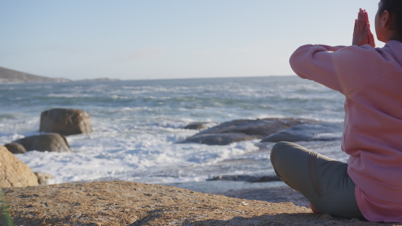 Meditating by ocean, mature asian woman practicing mindfulness on rocky shore
