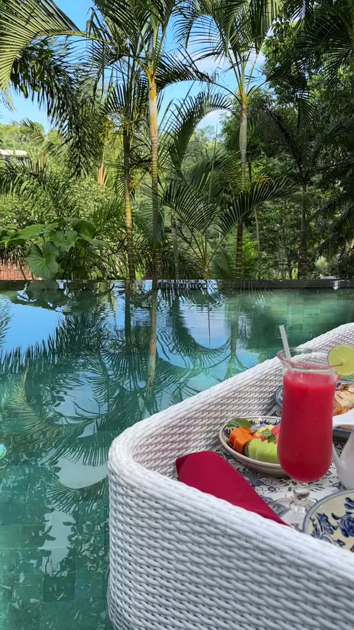 Enjoy a stunning vertical video of a floating breakfast tray on a serene pool, surrounded by lush tropical greenery in Bali. Perfect for mobile stories and social media sharing