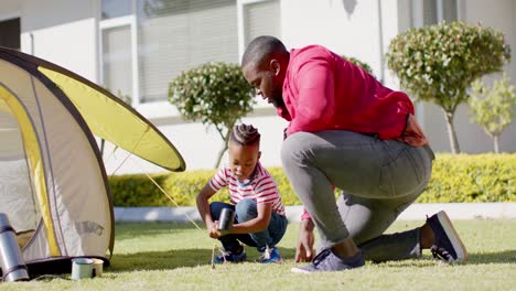 happy african american father and son pitching tent together in sunny garden, in slow motion