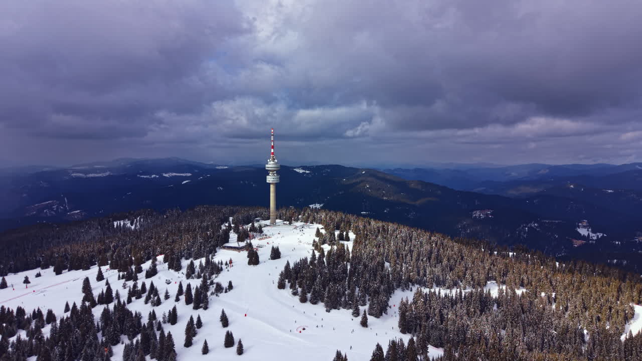 Area montuosa innevata con un'alta torre di comunicazione e colline distanti sotto cieli nuvolosi in inverno.