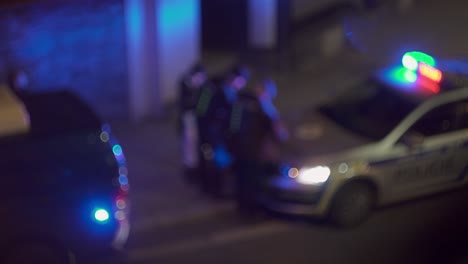 group of police officers around blinking cop car, beacon light, blurry night view