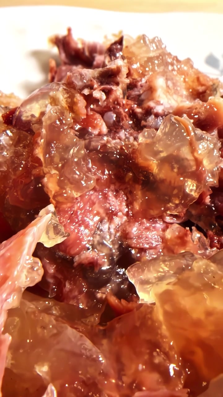 Carne di manzo tenera circondata da gelatina di aspic traslucida, adagiata su un piatto decorativo e illuminata da luce calda e naturale.