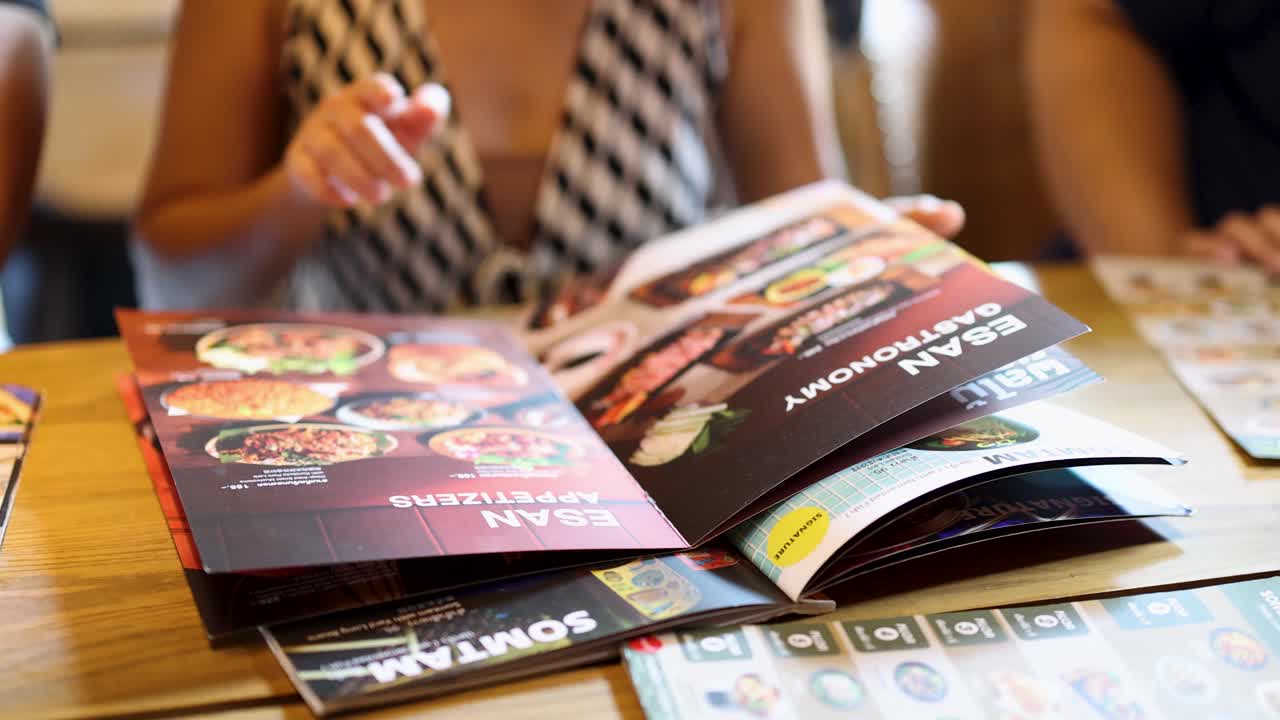 Woman flips through colorful Thai cuisine menu in bright restaurant, natural lighting, close-up view