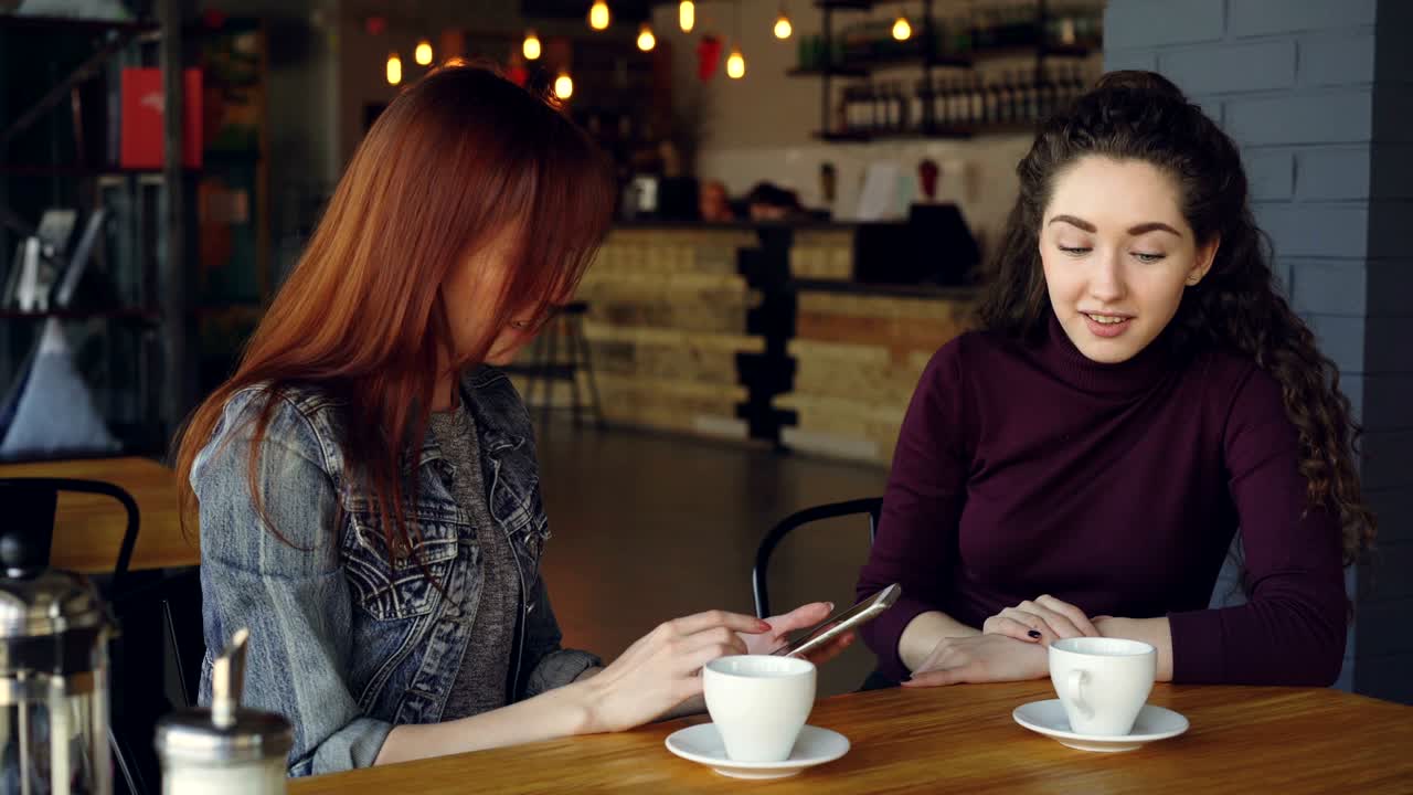 las mujeres jóvenes están usando teléfonos inteligentes, hablando y dando cinco mientras beben té en el café a la hora del almuerzo. comunicación, tecnología moderna, tiempo de chicas y concepto de personas felices.