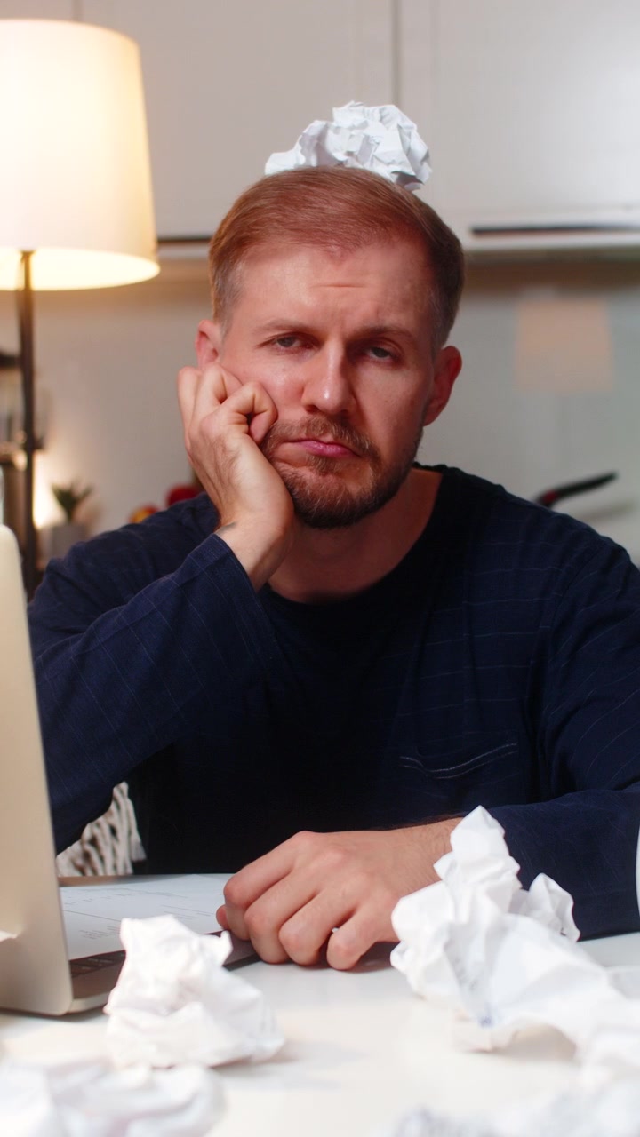 Young man struggles with ideas faces creative block writes notes crumpled paper critique morale low