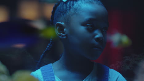 black girl looking at fish in aquarium curious child watching colorful sea life swimming in tank learning about marine animals in underwater ecosystem inquisitive kid at oceanarium