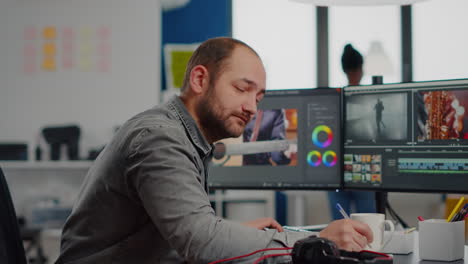 Videographer-smiling-at-camera-working-on-computer