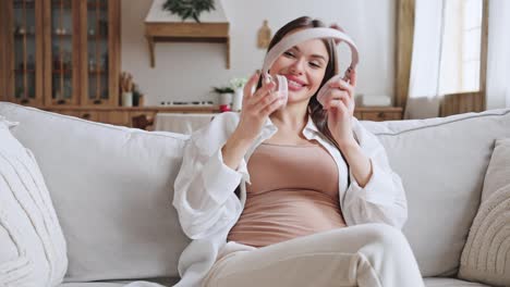 positive pregnant woman listens to music sitting on sofa