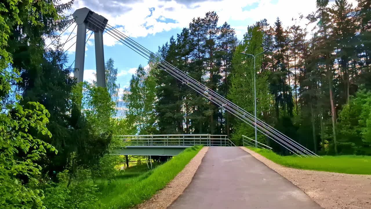 Modern cable-stayed footbridge with metal supports and forest path in Valmiera, Latvia