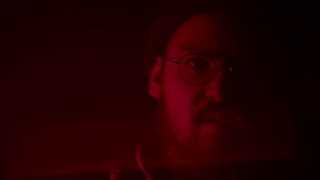 un homme avec des lunettes et une barbe dans la lumière rouge