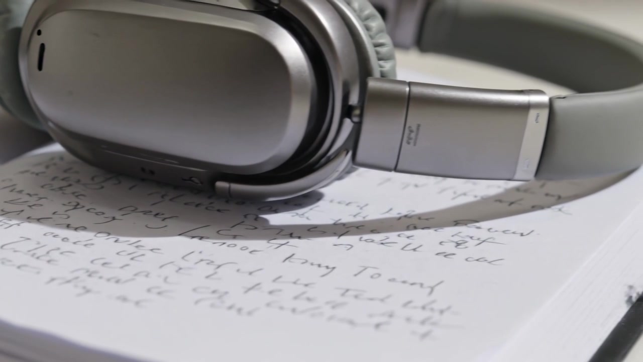 Sliding camera moving right and closer, revealing silver headphones on open notebook showing notes