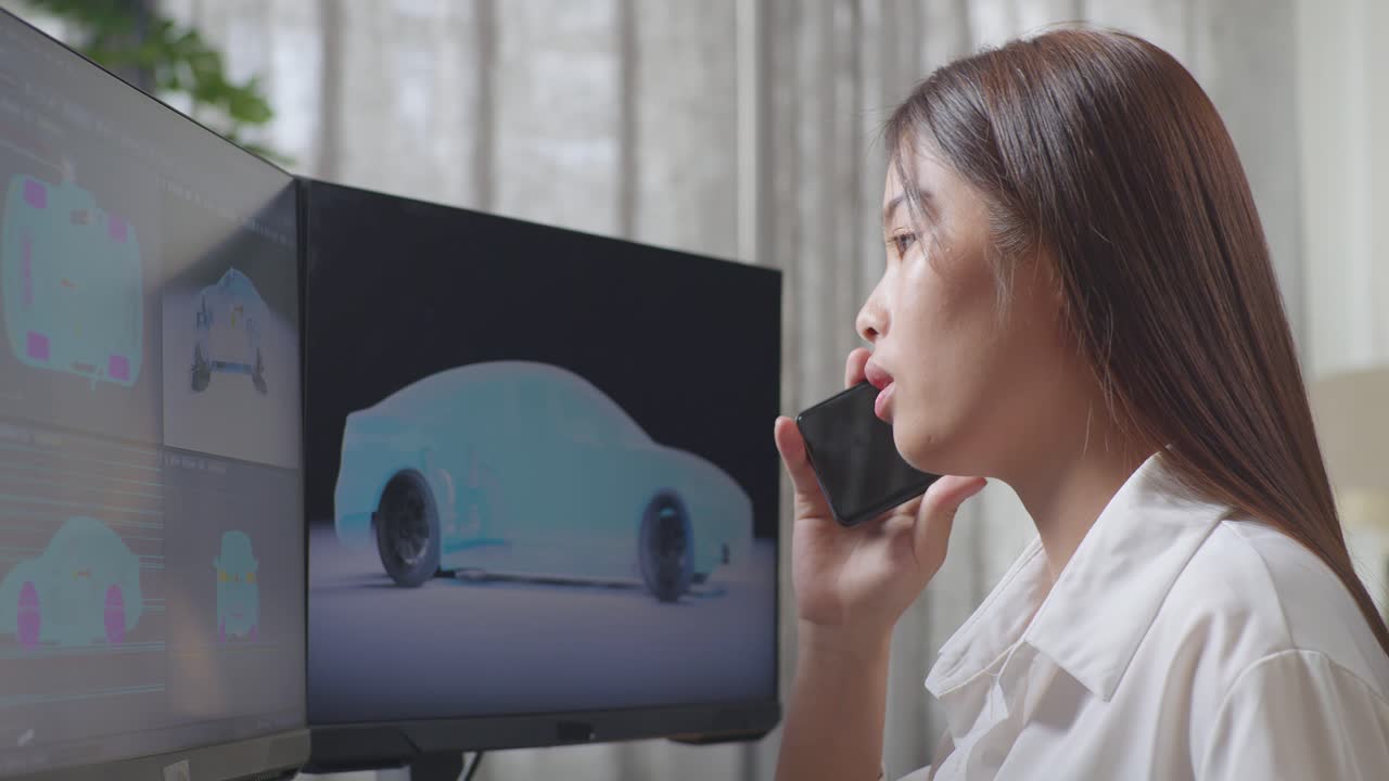 아시아 여성 자동차 디자이너가 스튜디오의 데스크 컴퓨터에서 ev 자동차의 3d 모델을 작업하는 동안 스마트폰에서 이야기하는 가까운 측면 뷰
