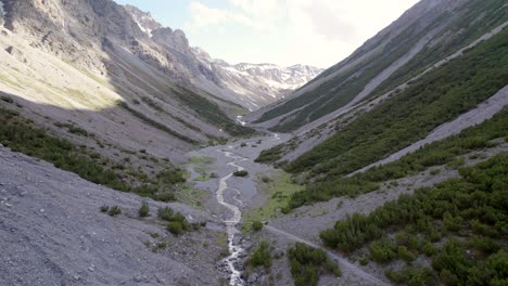 aerial drone footage reversing upwards through a dramatic glacial valley surrounded by a steep mountains and pine trees with patches of snow and an alpine river in switzerland