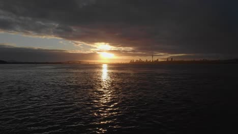 vuelo aéreo bajo y elevándose sobre el puerto de auckland con el paisaje urbano del amanecer dorado