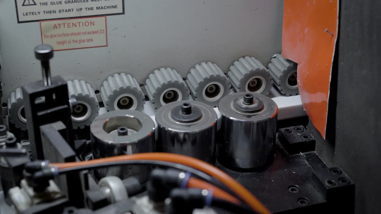 los rodillos están pegando el panel de plástico al borde de la placa de partículas, vista interior en la máquina de borde industrial