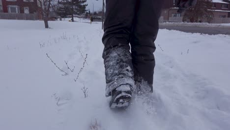 young child walking in snow alongside road wearing grey snowpants boots gloves in winter