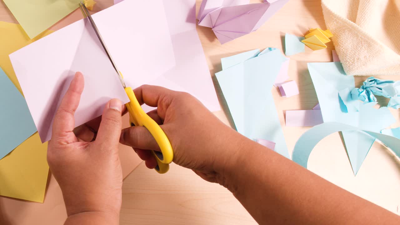 Primo piano dall'alto di mani che usano forbici gialle per tagliare la carta per un progetto di origami