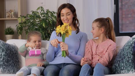 Daughters-Giving-Flowers-and-Gift-to-Happy-Mother.people,-family-and-holidays-concept-two-daughters-giving-flowers-and-present-to-happy-mother-at-home