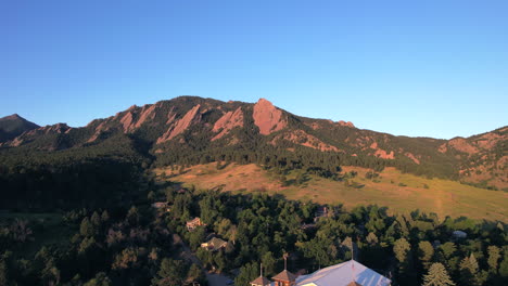 Drone-rising-up-in-chautauqua-park-revealing-the-flatirons-nature-area-and-houses-during-sunrise-on-a-summer-morning