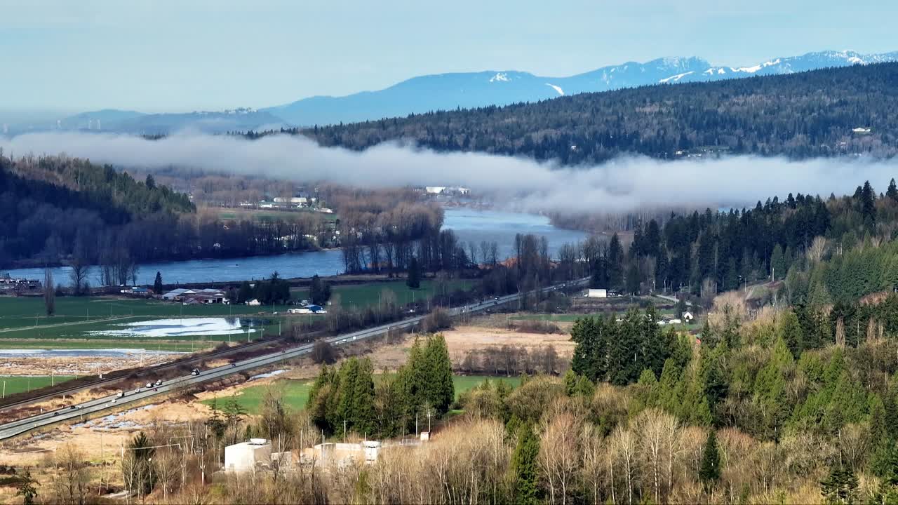 Clouds Over Fraser River And Mountains With Pine Trees In Mission, British Columbia, Canada. - aerial shot