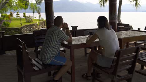 a man with a woman is sitting at a table overlooking the lake and mountains