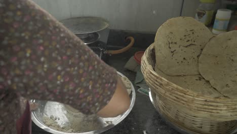 over the shoulder shot of a senior aged woman making traditional bhakri in indian kitchen using cooking gas stove