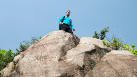 A-man-free-climber-standing-on-top-of-a-mountain-with-outstretched-arms-and-enjoying-the-view,-low-angle-view-against-blue-sky