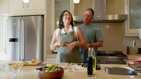 senior diverse couple preparing fresh salad together in modern kitchen, enjoying cooking, at home