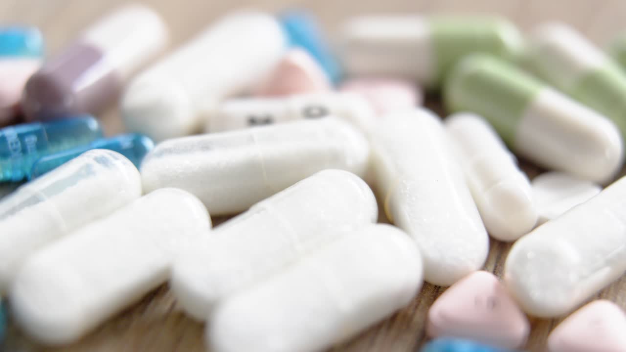Assorted pills and capsules scattered on a wooden surface in close-up view