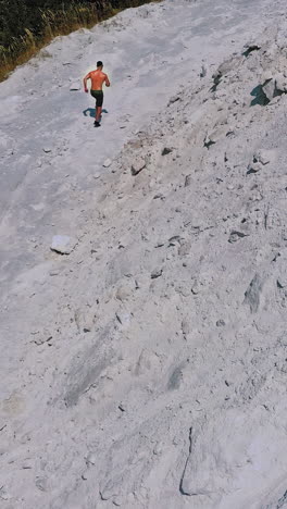top view on a sportsman in the mountains. shirtless athlete is running on the white hill background in summer. aerial view. vertical video