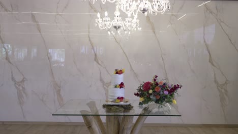 wedding cake and floral arrangement on glass table under chandelier in elegant venue
